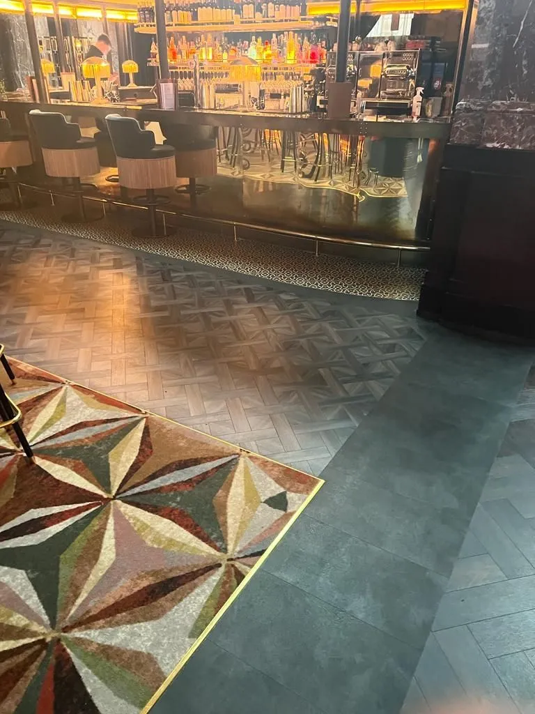 Basket-weave Amtico in front of the main bar, between a brass-edged inset carpet and a dark tile-effect vinyl border