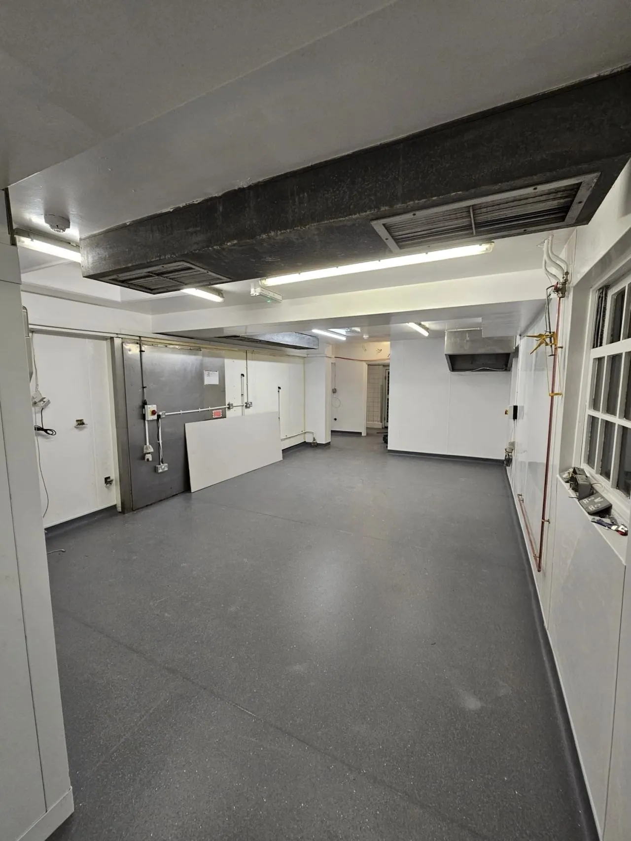 Grey safety sheet vinyl coved up the walls of an empty basement kitchen
