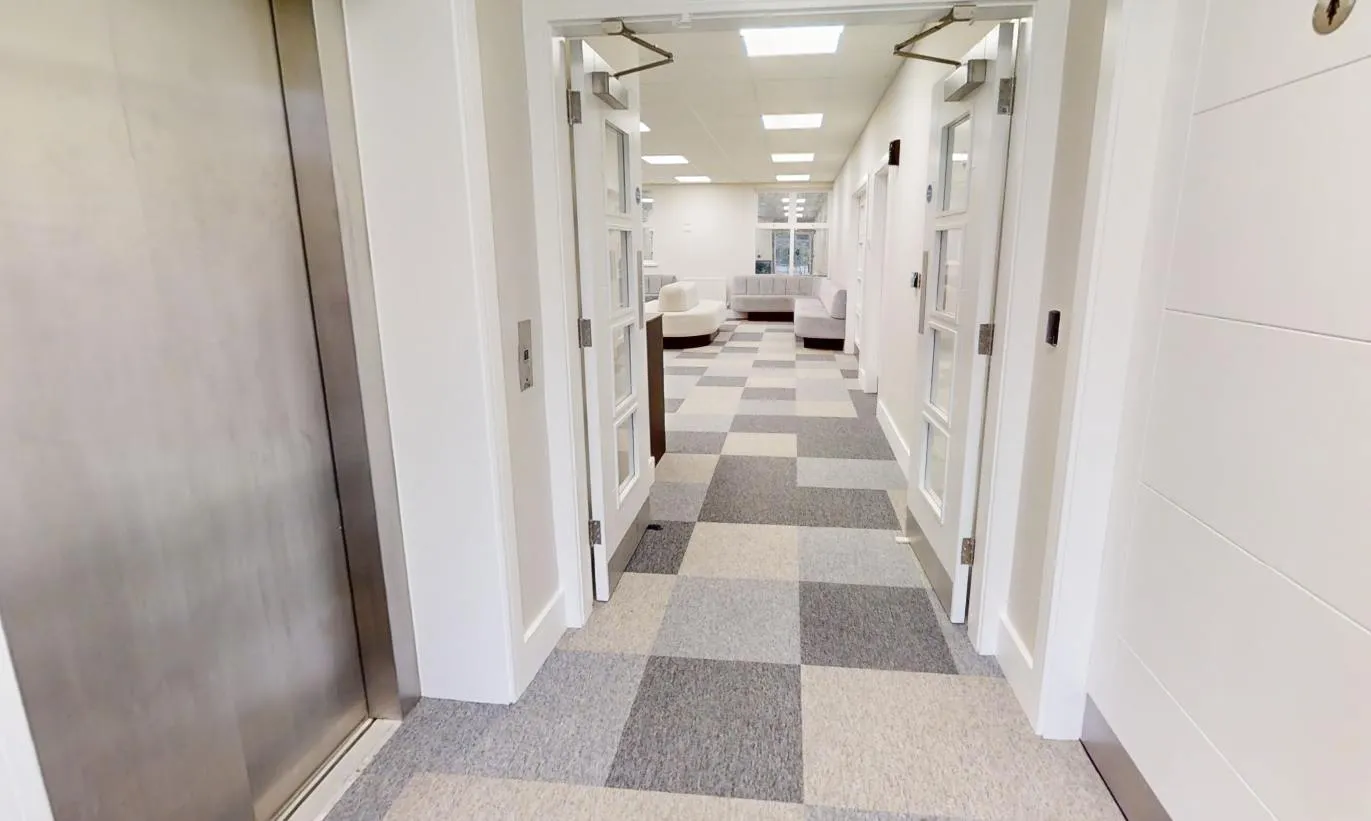 Carpet-tiled corridor in mixed grey and oatmeal tones, running from the lift at Abbey House Dental