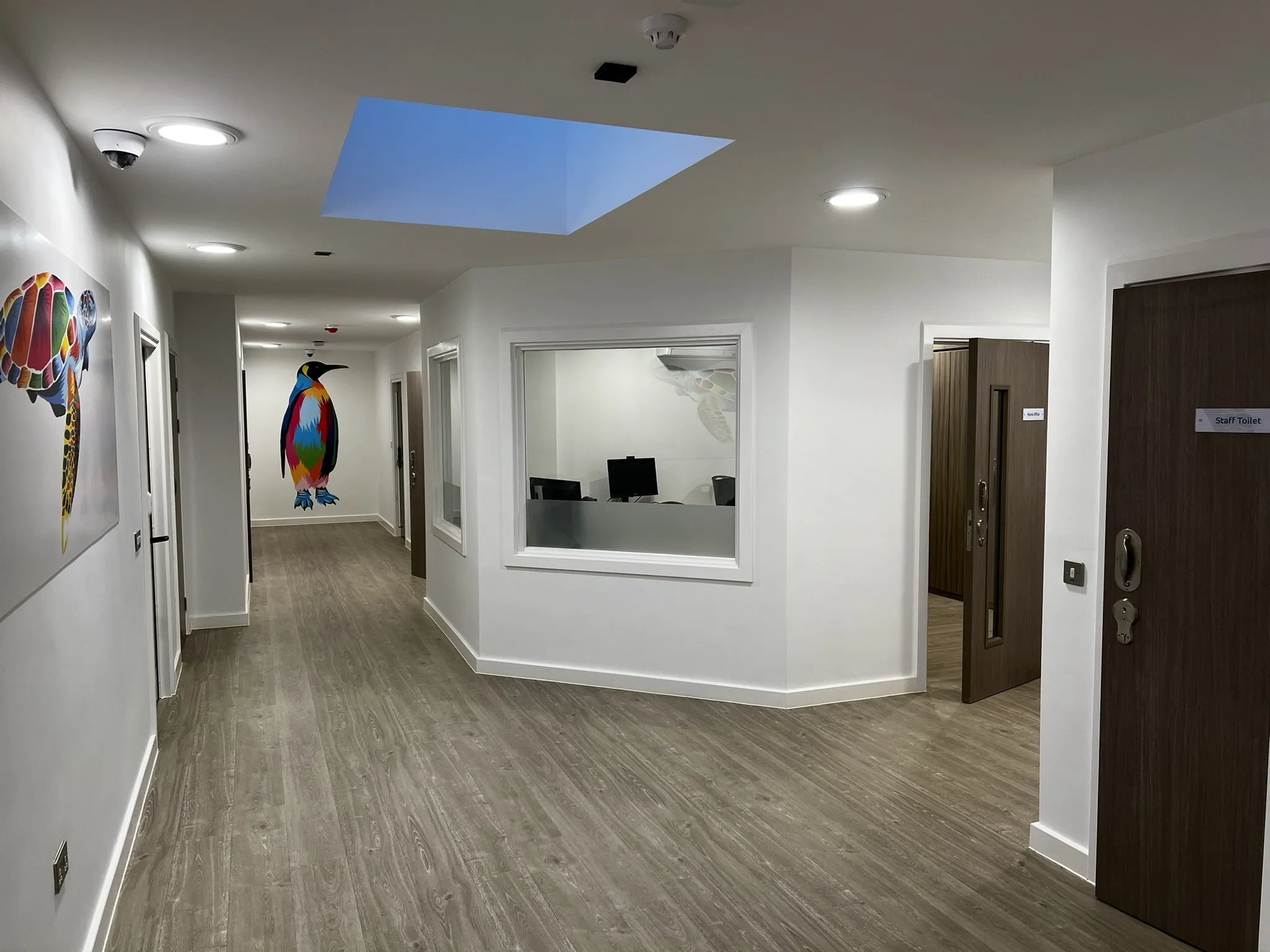 Polyflor Wood FX safety vinyl along a corridor at Emerald Place Clinic, past an office window towards a penguin mural