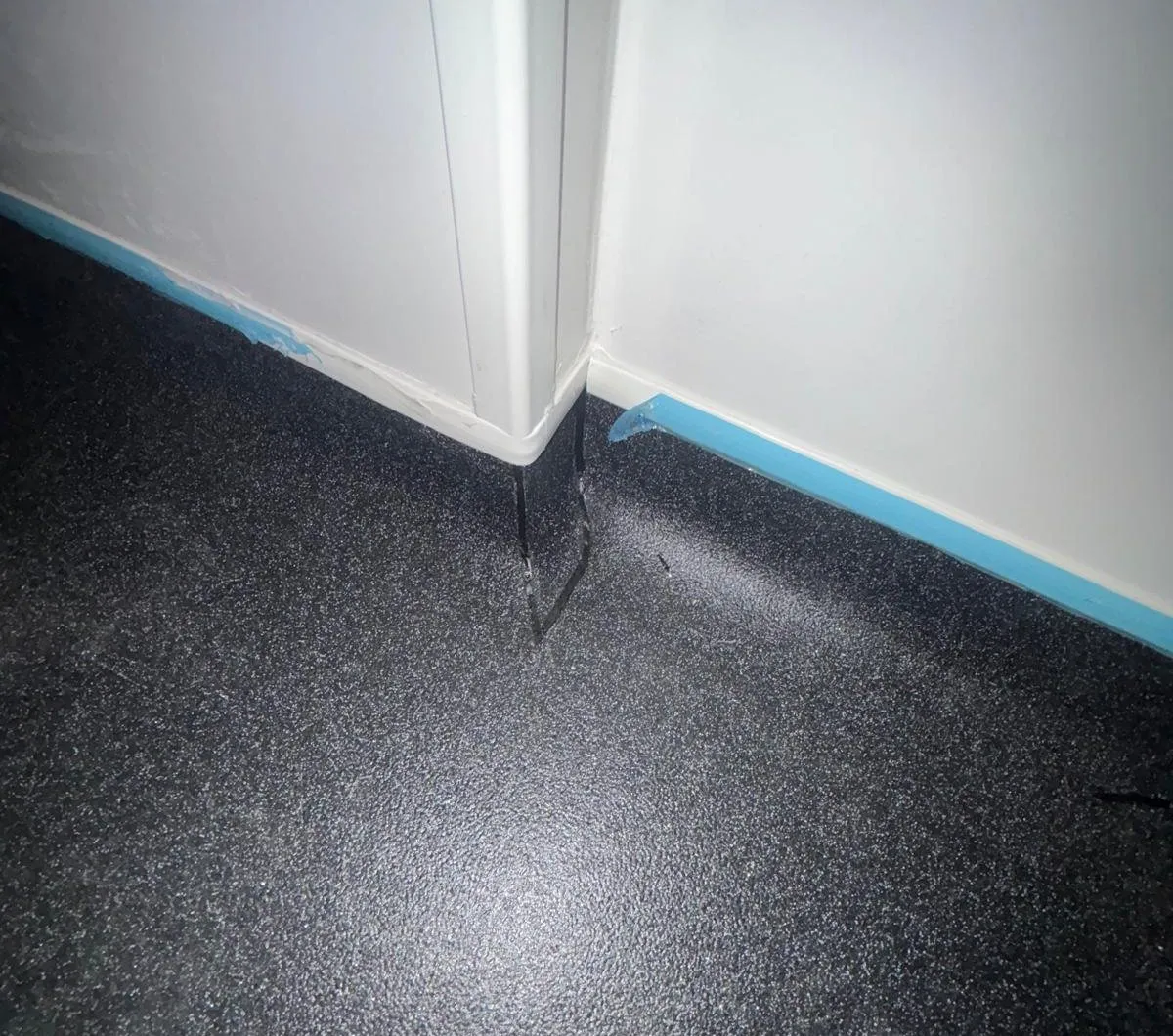 Black safety vinyl formed around an external corner of the wall cladding and coved up both walls