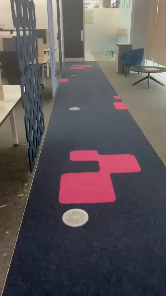 A pink inlay beside a floor box in the navy walkway, with grey carpet and desks either side