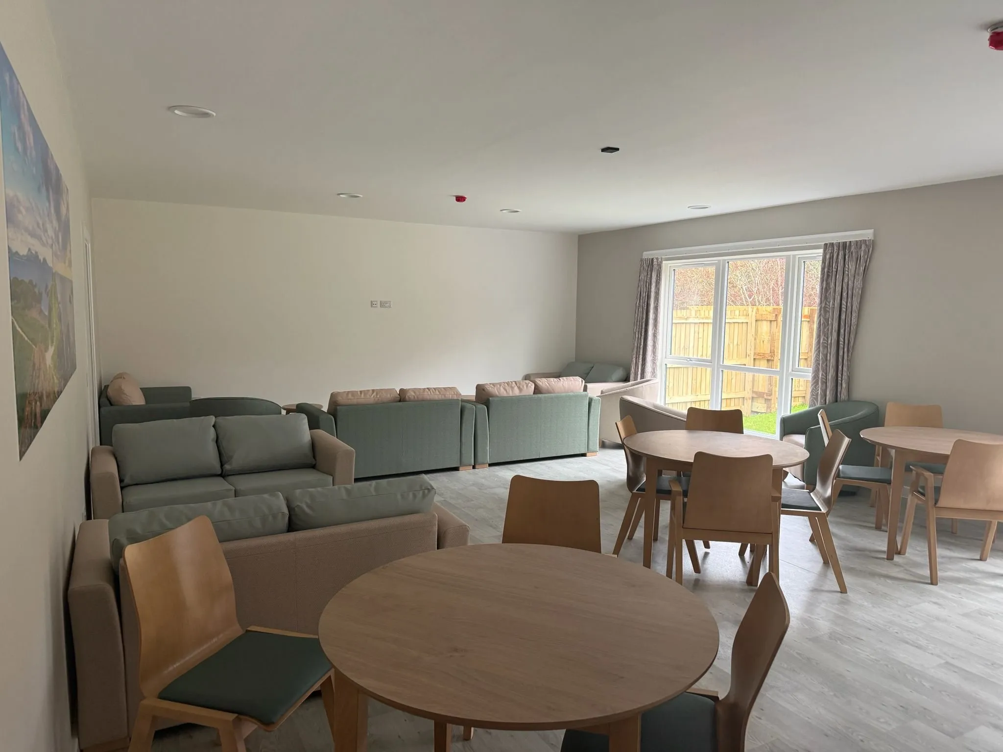 Wood-effect sheet vinyl through a lounge and dining room, with sofas and round tables by the garden window