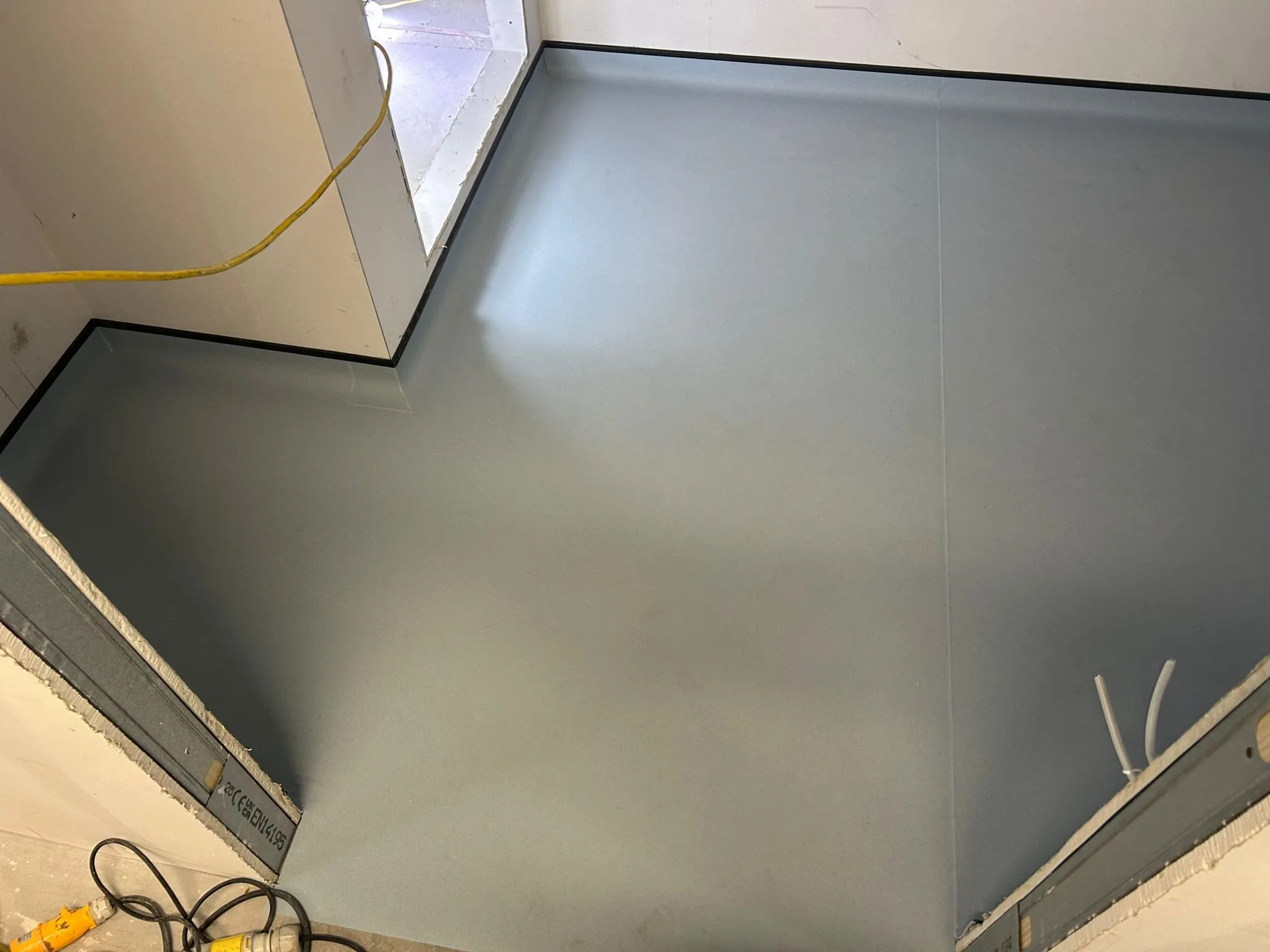 Grey-blue sheet vinyl coved up the walls and finished with a black capping strip around an L-shaped room in a modular hospital building