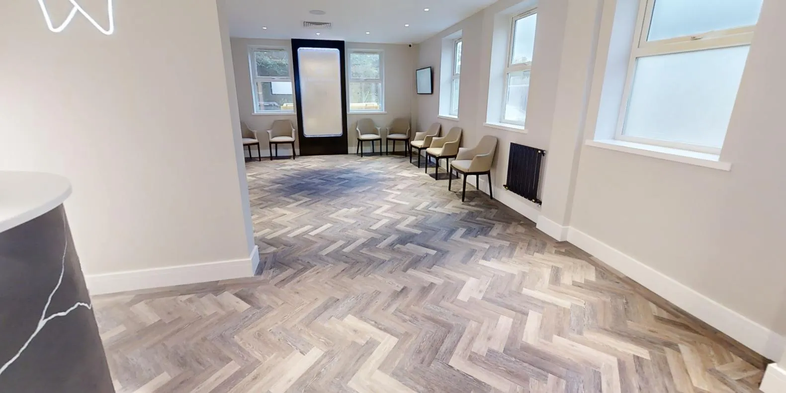 Herringbone LVT flowing from reception into the waiting area at Abbey House Dental, edged with a border plank along the walls