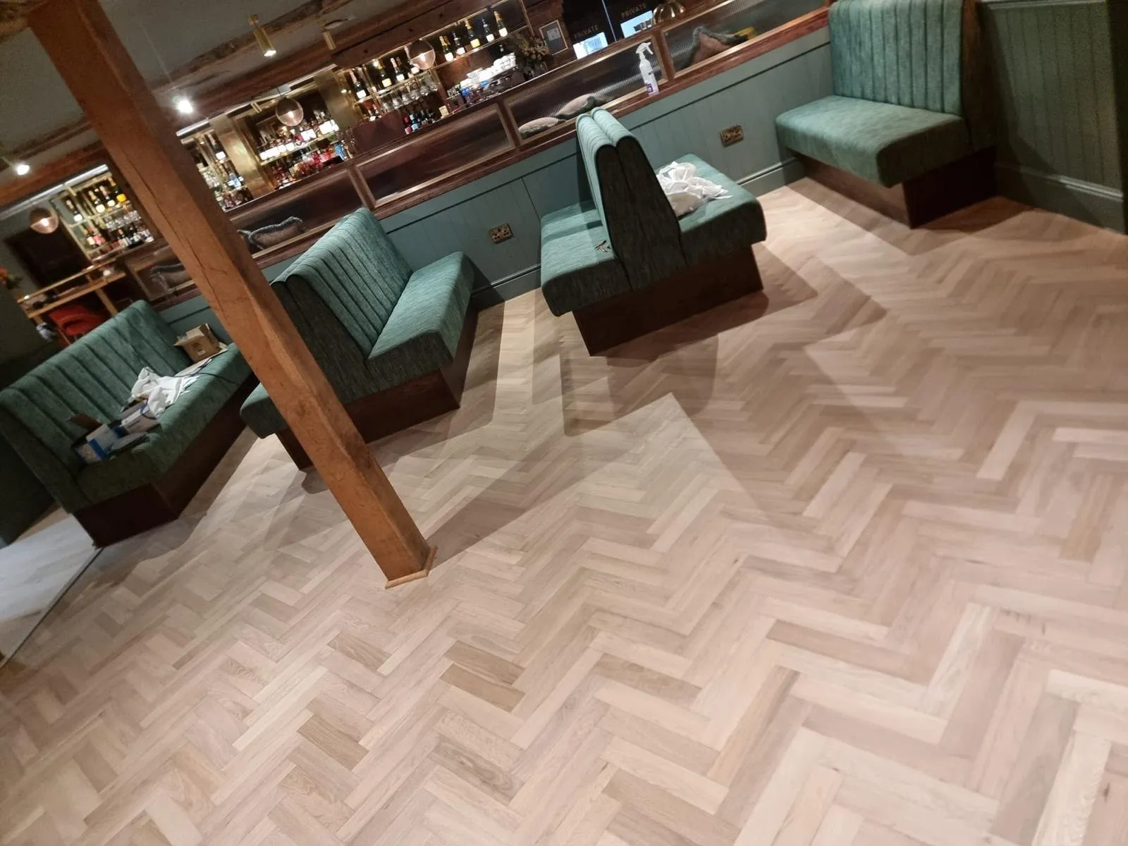 Light oak herringbone around green velvet booths in the bar lounge of a restaurant in Exeter