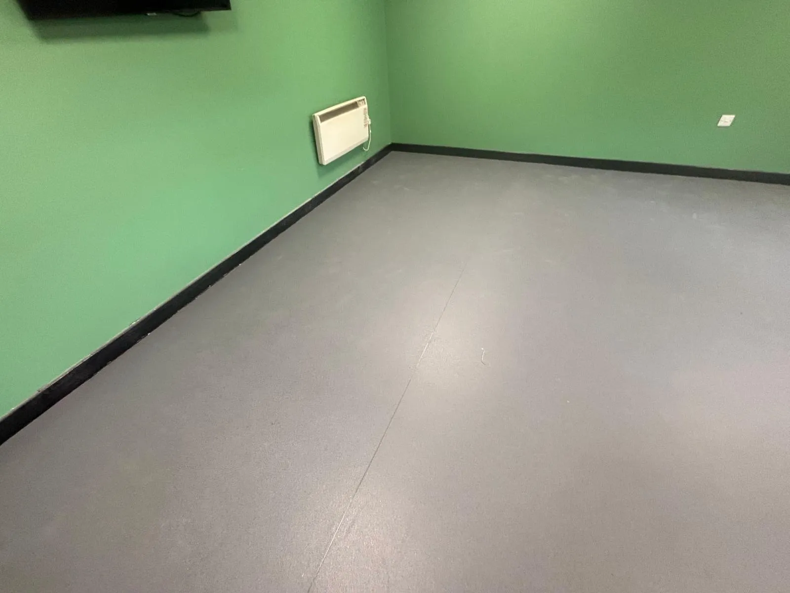 A straight run of black skirting along two walls, meeting grey sheet vinyl, in a back-of-house room at Roadchef Chester