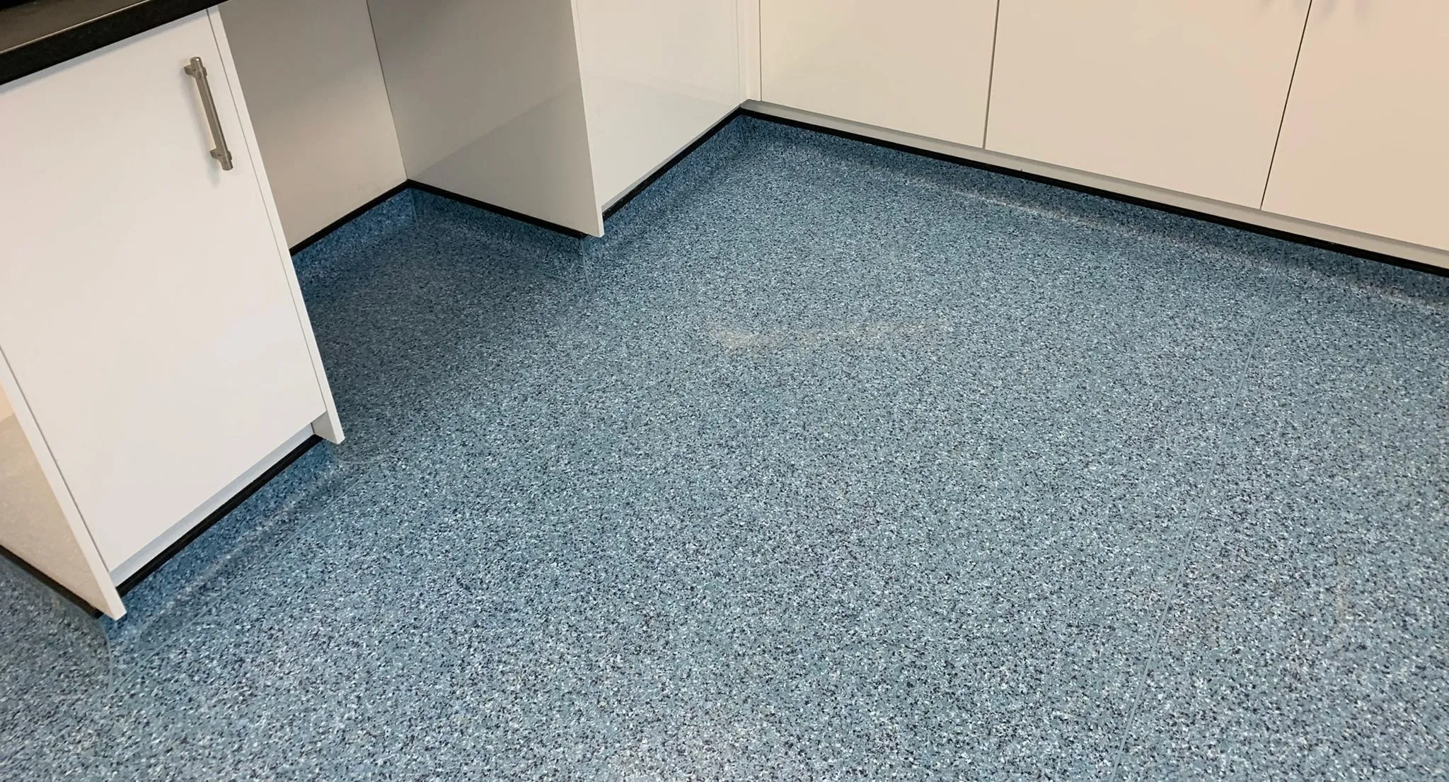 Blue speckled safety vinyl coved up into the recesses and around the base units of a staff kitchen, finished with a black capping strip