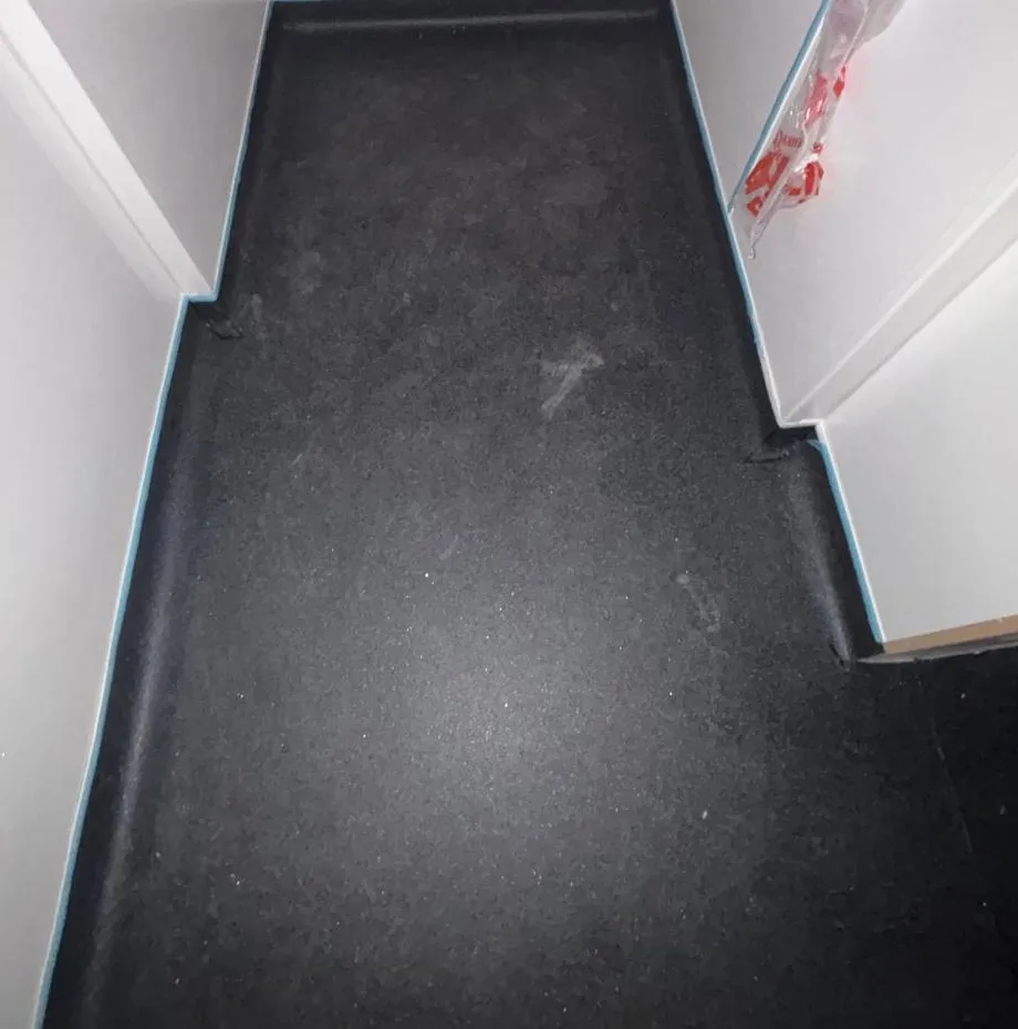 A back-of-house store room in black safety vinyl, coved up the walls on every side, before the protective film came off the cladding
