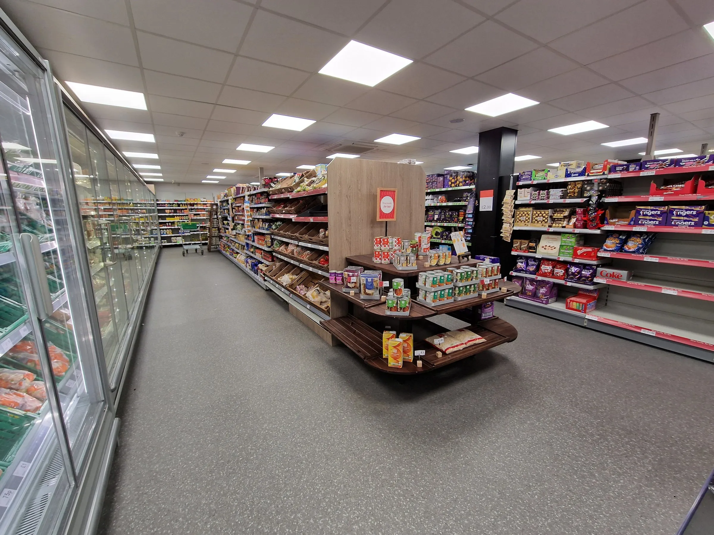 Grey speckled safety vinyl running the length of a convenience store, past the chiller wall and a timber display unit