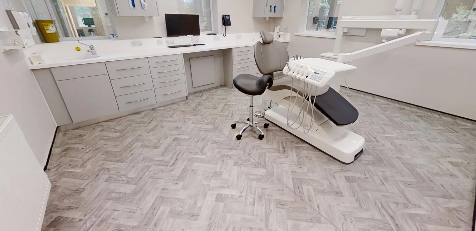 Treatment room with pale herringbone-effect sheet vinyl beneath the clinical cabinetry