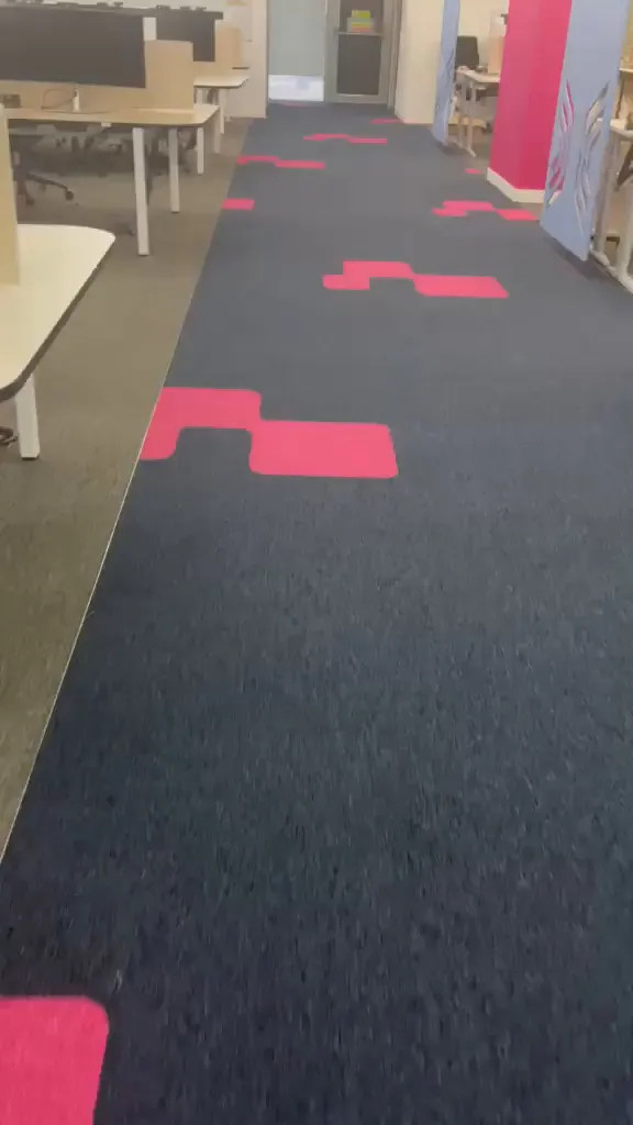 Navy carpet tile walkway with pink inlays running between rows of desks